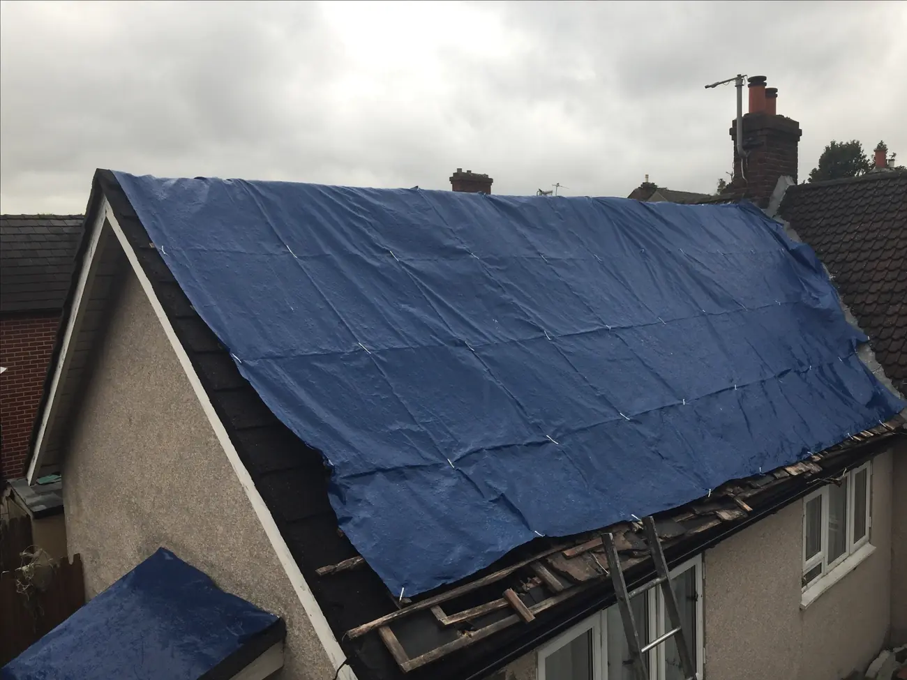 Tarpaulin battened over storm-damaged tiles on a pitched roof