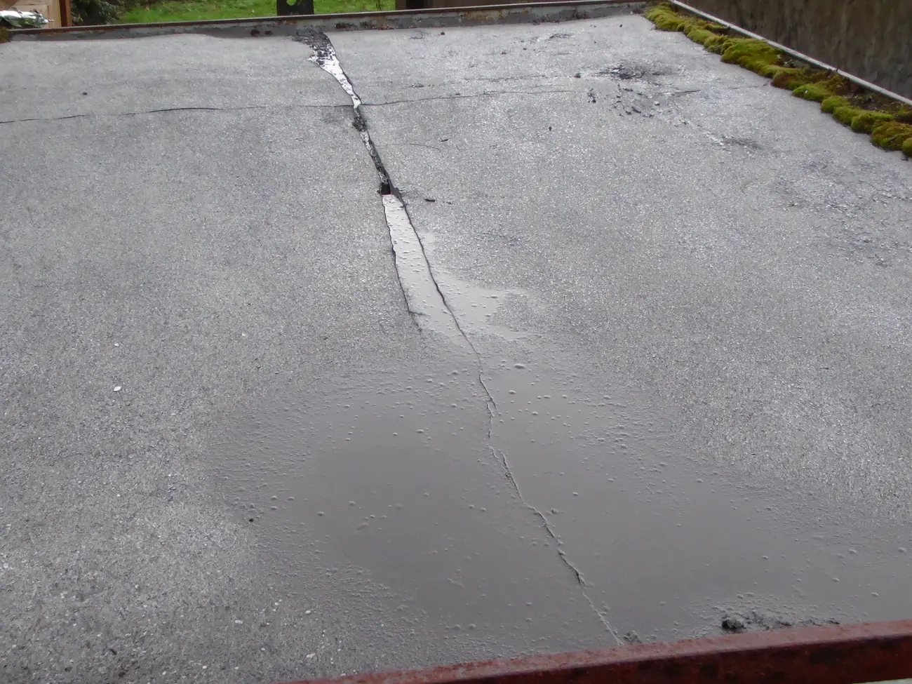 Split felt and standing rainwater ponding on an old garage flat roof