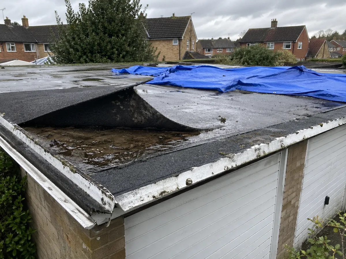 Torn felt flat garage roof with blue tarp after storm damage in Stowmarket