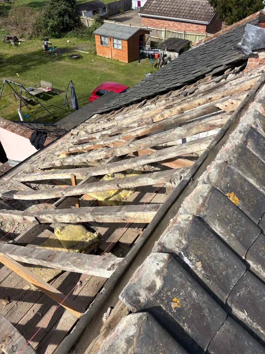 Roof slope stripped of its old tiles back to the battens, with the hip tiles still in place