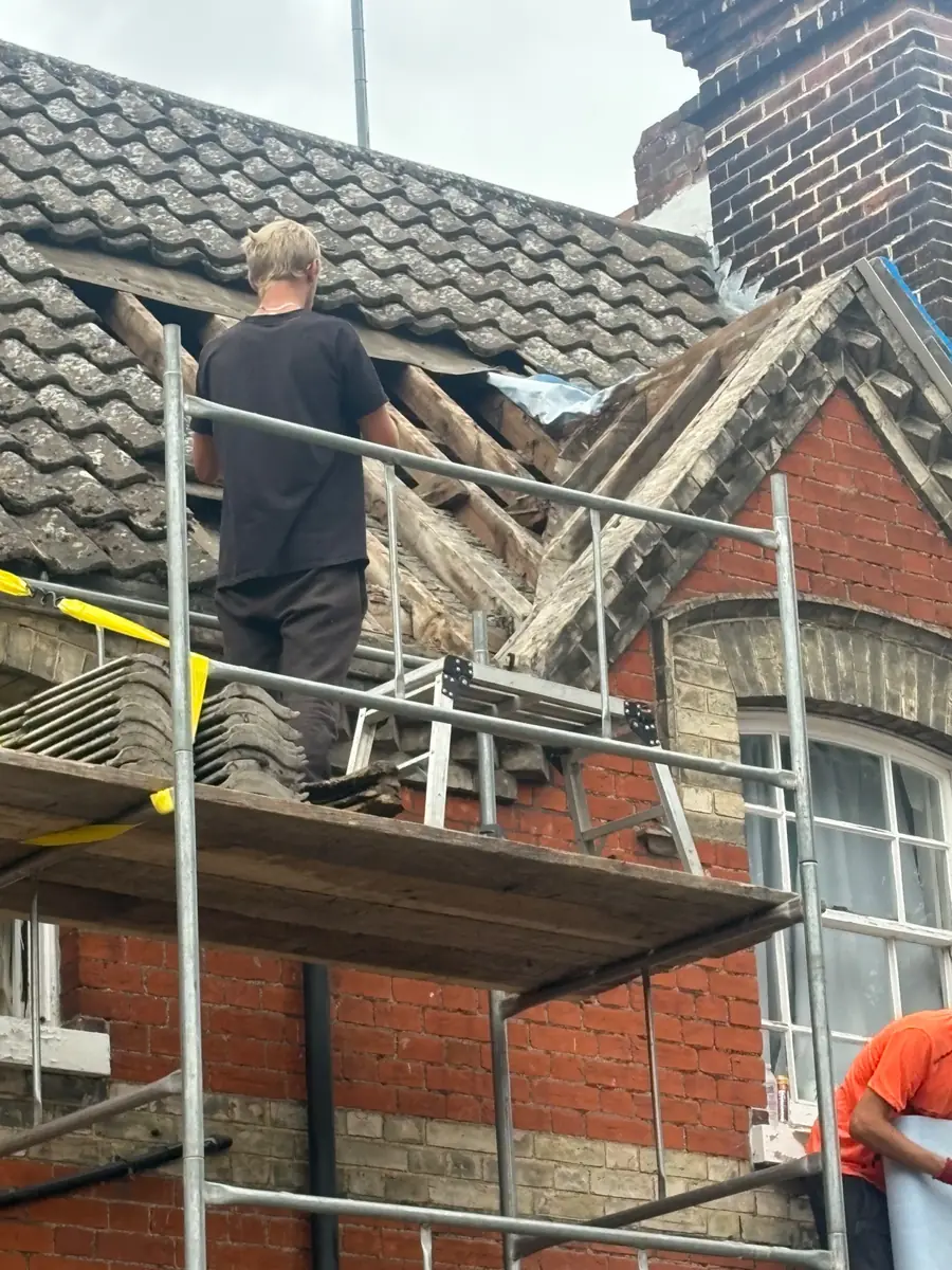 Stormproof roofer on the scaffold stripping old tiles and timbers from a gable on a red brick house